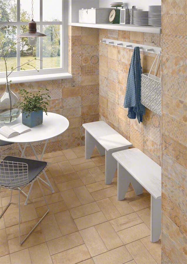 Una habitación con paredes y suelo de azulejos color canela. Bancos blancos, perchero, mesa y ventana.