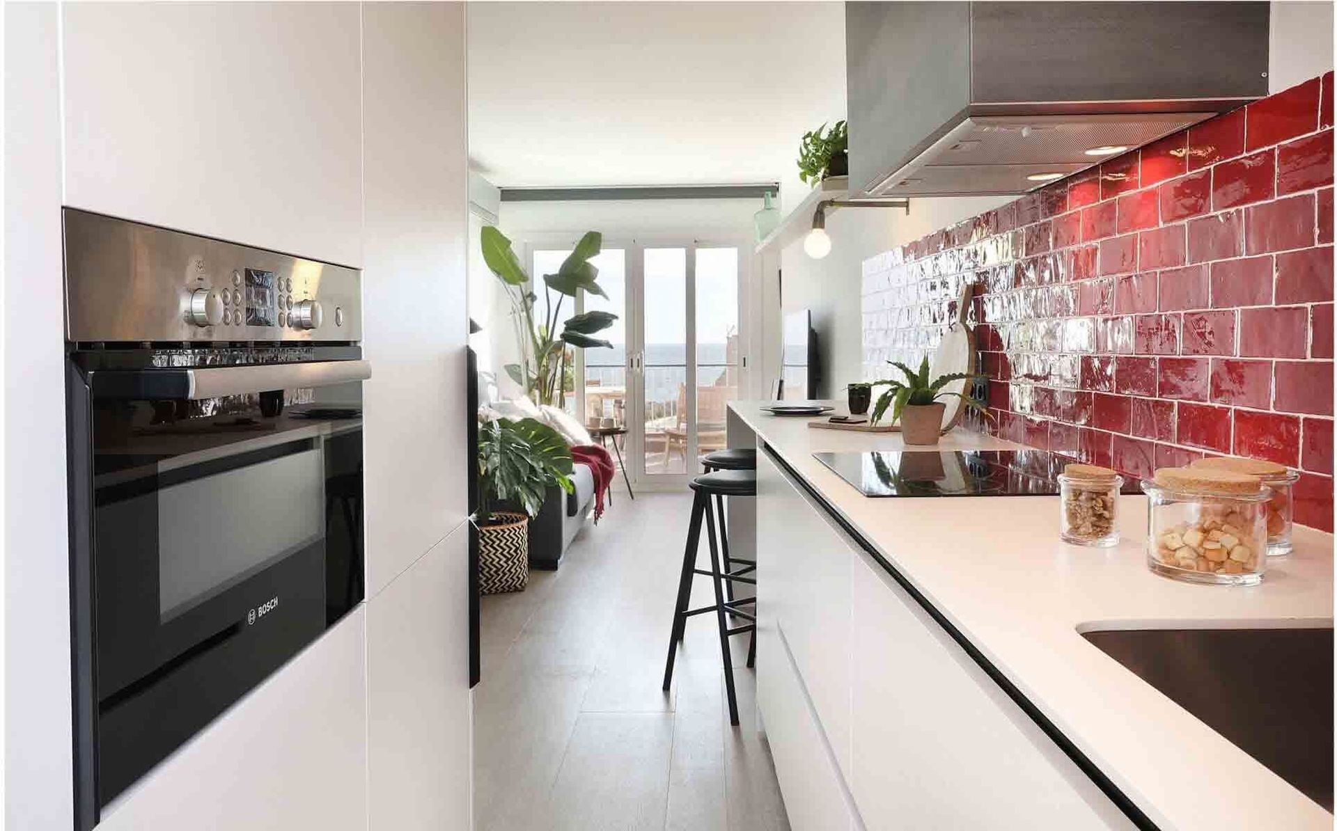 Cocina moderna con salpicadero de azulejos rojos, encimeras blancas y electrodomésticos de acero inoxidable.