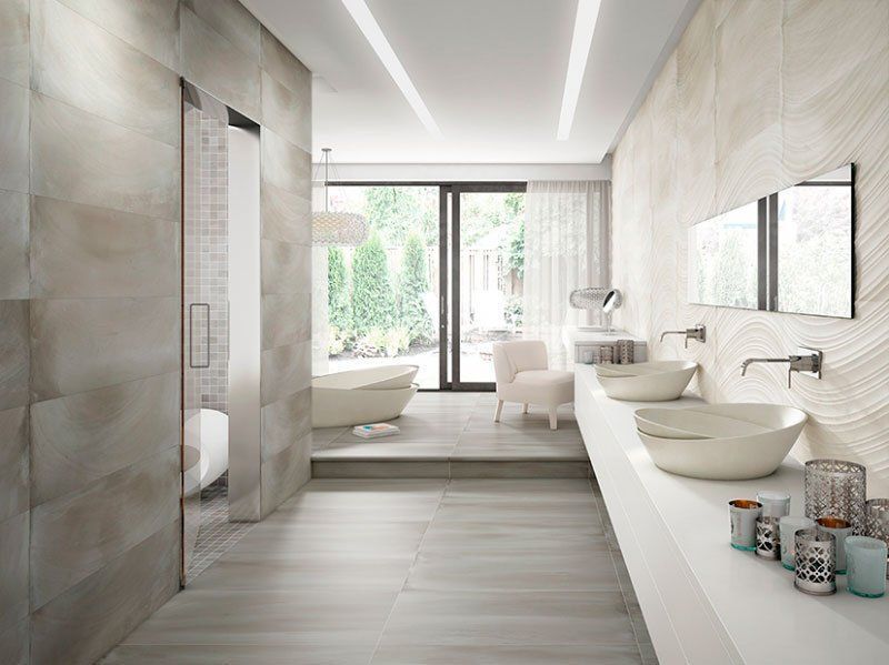 Baño moderno con azulejos de colores claros, una ventana grande, una bañera independiente y un tocador doble con lavabos tipo vasija.