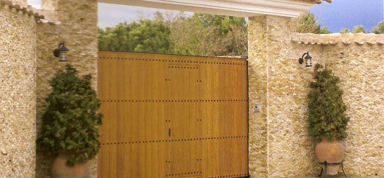 Puerta de madera y muros de piedra con plantas en macetas a ambos lados.