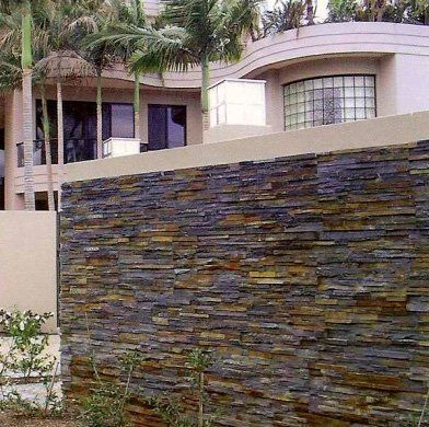 Muro de piedra frente a un edificio moderno con palmeras.