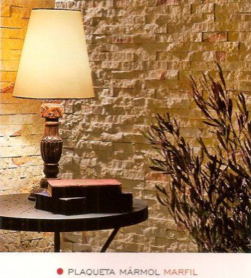 Lámpara sobre mesa pequeña frente a pared de mármol texturizado; planta a la derecha, libros debajo.