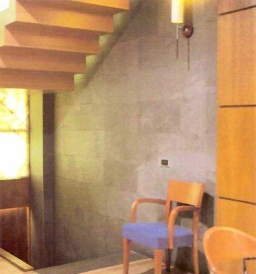 Escalera de madera sobre una silla con asiento azul contra una pared de piedra, con iluminación cálida y un armario de madera.