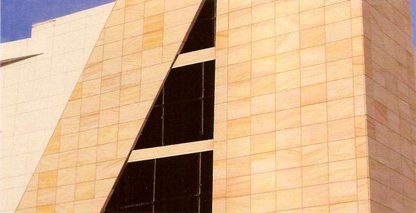 Edificio de piedra beige con una gran ventana de cristal triangular.