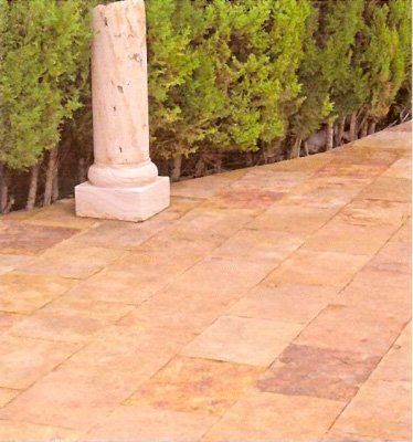 Columna de piedra sobre patio de baldosas, fondo de seto verde.