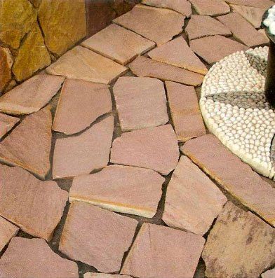 Patio de losas irregulares de color rojizo con borde de mesa de guijarros de mosaico.