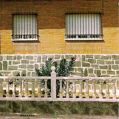 Dos ventanas con rejas de seguridad en un edificio de ladrillo con pared de piedra y barandilla ornamentada.