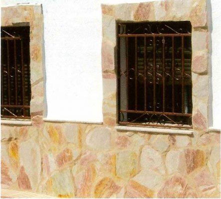 Ventanas con rejas de seguridad marrones en un edificio de piedra, pared blanca.
