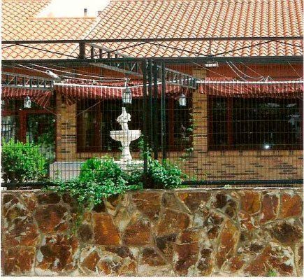 Edificio con techo de tejas rojas, muro de piedra y fuente al frente.