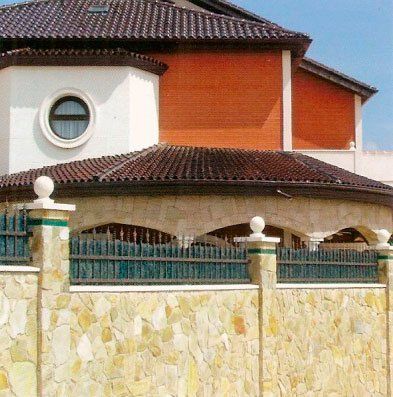 Casa con muro de piedra y valla decorativa; tejado marrón, fachada naranja y blanca.