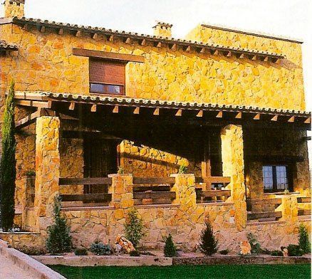 Casa de piedra con porche de madera, techo marrón y pequeñas plantas en el frente.