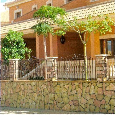 Casa con muro de piedra y verja de forja, con arboleda y porche.