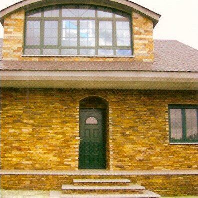 Casa de ladrillo amarillo con marcos de puertas y ventanas de color verde oscuro; escalones conducen a la entrada.