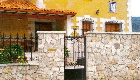 Casa de estuco amarillo con valla de piedra y puerta de hierro forjado.