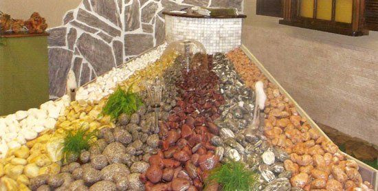 Exhibición de guijarros multicolores, que se asemeja a una cascada, con un fondo con textura de piedra.