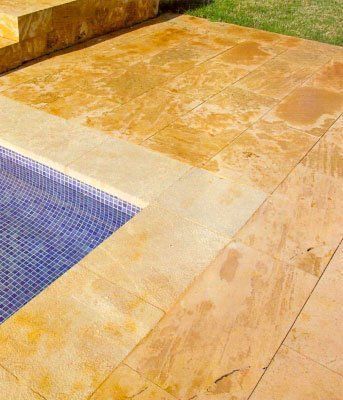 Vista de la piscina con azulejos de piedra en tonos dorados e interior de piscina de mosaico azul.