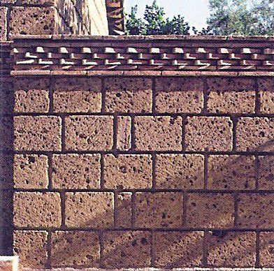 Muro de piedra con molduras decorativas de ladrillo, tonos marrones, posiblemente un edificio exterior.