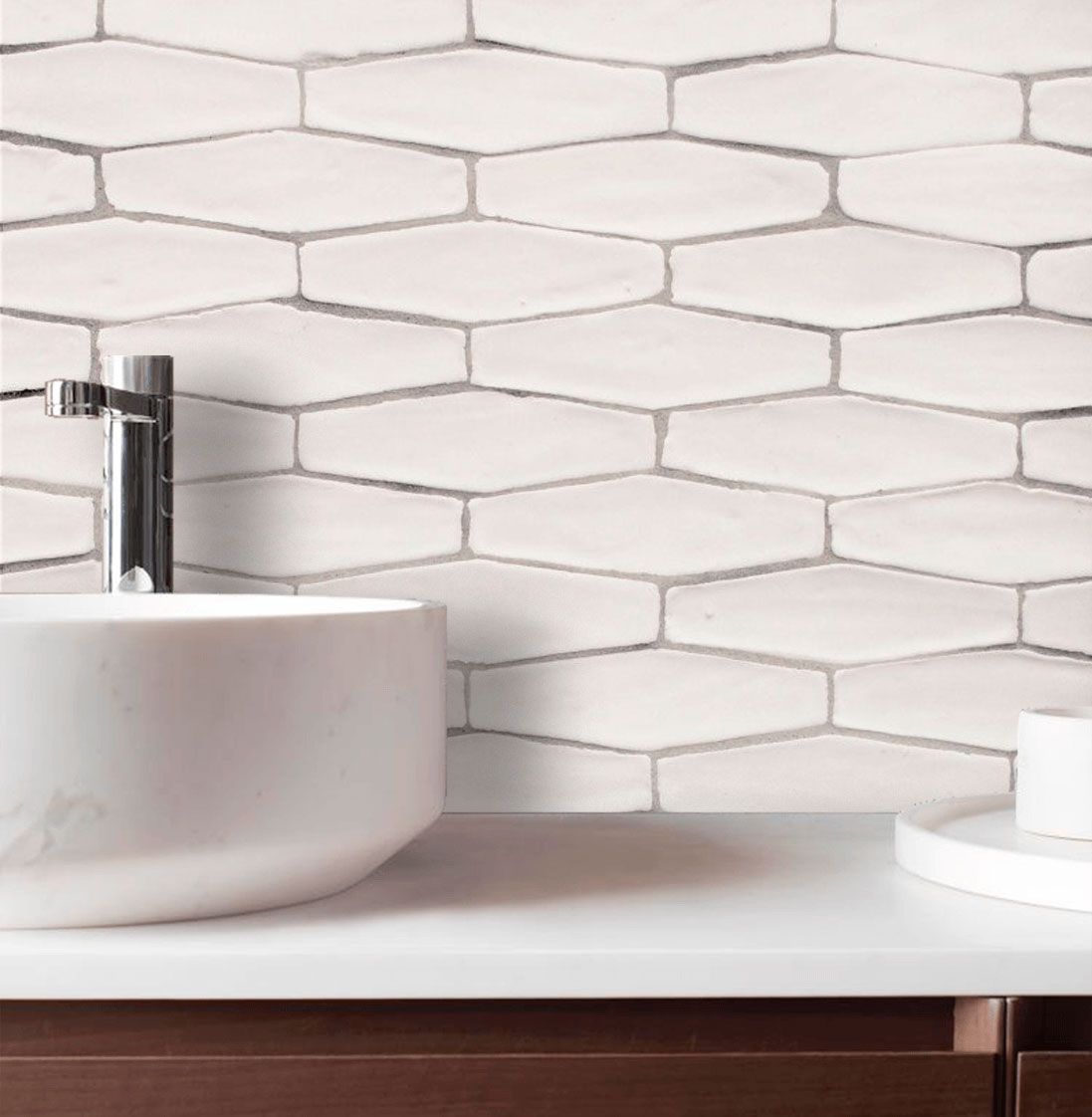 Baño blanco con salpicadero de azulejos de forma ovalada, lavabo blanco, grifo cromado y mueble de madera.