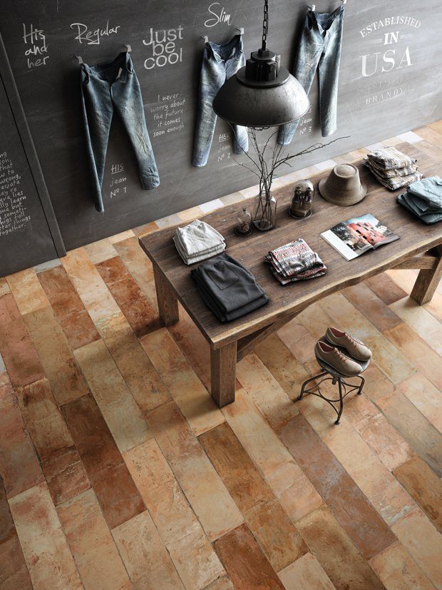Un expositor minorista con pantalones vaqueros colgados en una pared de pizarra, una mesa de madera con ropa doblada y un piso con apariencia de madera.