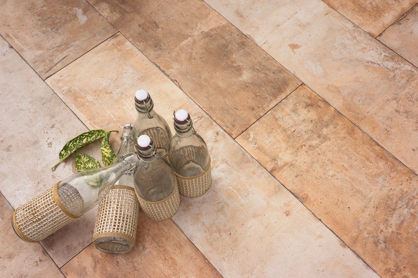 Botellas de vidrio con mangas tejidas y hojas verdes sobre una superficie de baldosas de piedra.