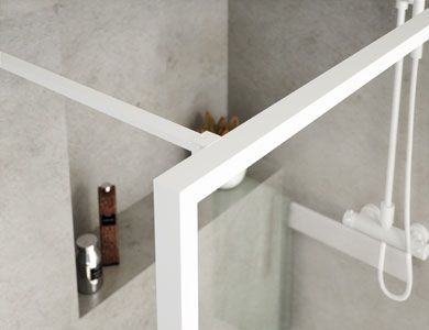 Marco de ducha blanco en esquina, con mampara de cristal. Un pequeño estante para artículos de aseo.