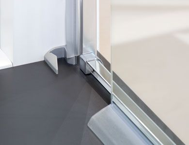 Marco de puerta de ducha de metal plateado unido a un piso gris oscuro y una pared blanca.