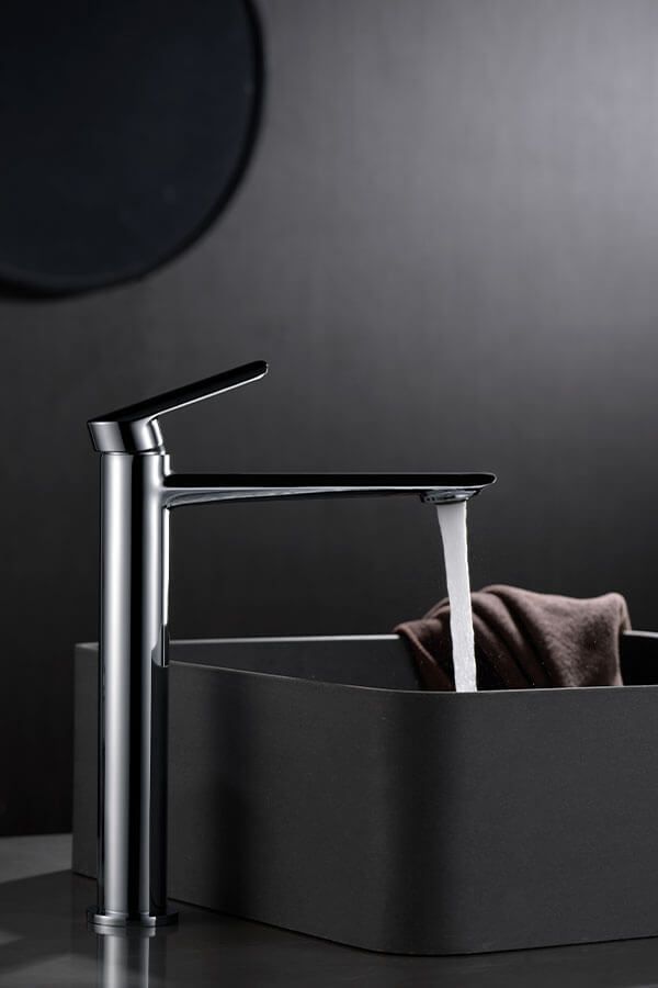 Grifo alto cromado que vierte agua en un lavabo gris oscuro, con una toalla dentro; fondo negro.
