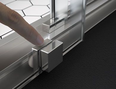 Dedo tocando el tope metálico de una puerta corrediza de ducha, al lado de un suelo negro y baldosas blancas en forma de panal.