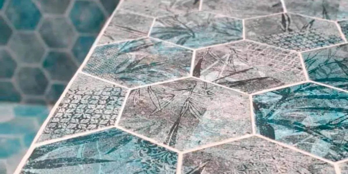 Primer plano de la superficie de una mesa con baldosas hexagonales. Las baldosas son de color aguamarina, gris y blanco con un estampado de hojas.