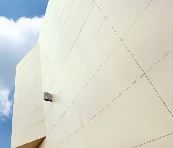 Fachada de edificio color crema contra un cielo azul parcialmente nublado. Una lámpara cuadrada está fijada a la pared.