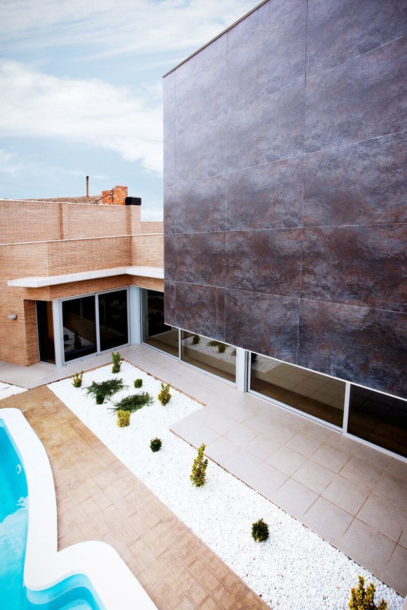 Edificio moderno con fachada de piedra marrón, piscina y estructura de ladrillo en un día soleado.