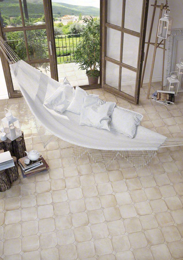 Una hamaca blanca con almohadas en una habitación soleada, con puertas abiertas a un jardín. Suelo de baldosas beige.