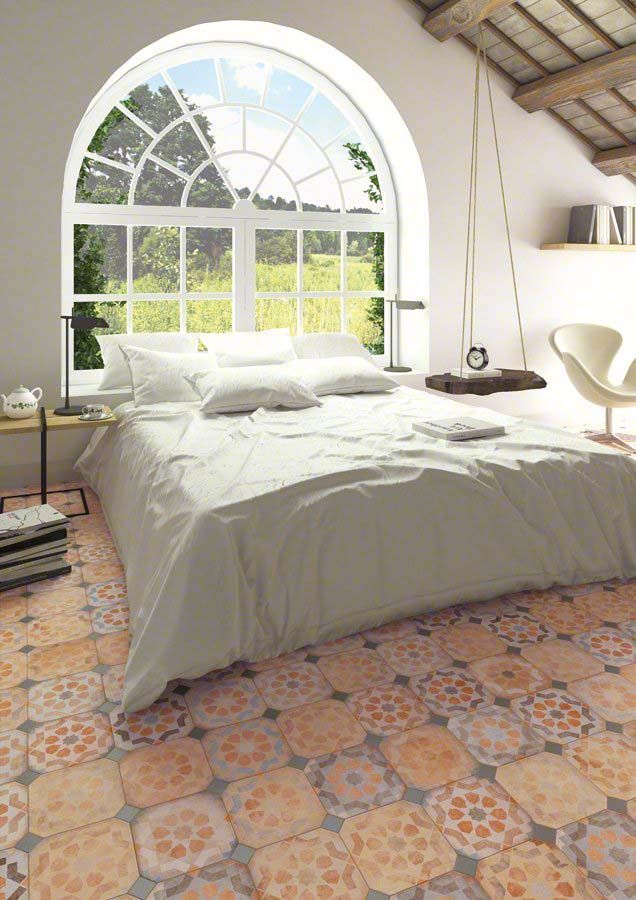 Dormitorio con ventana arqueada con vistas a un paisaje verde. Cama con ropa de cama blanca y suelo de baldosas estampadas en naranja y gris.