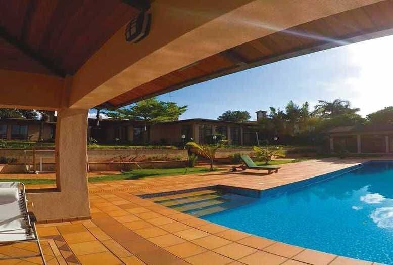 Vista a la piscina con piscina, tumbona, césped y edificios bajo un cielo soleado.