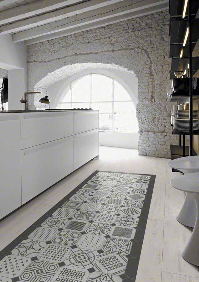 Cocina con gabinetes blancos, arco de piedra, corredor de azulejos estampados y piso de madera clara.