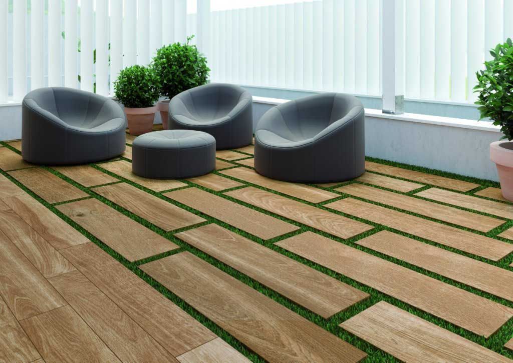 Patio al aire libre con baldosas de apariencia de madera y franjas de césped, asientos grises y plantas en macetas.