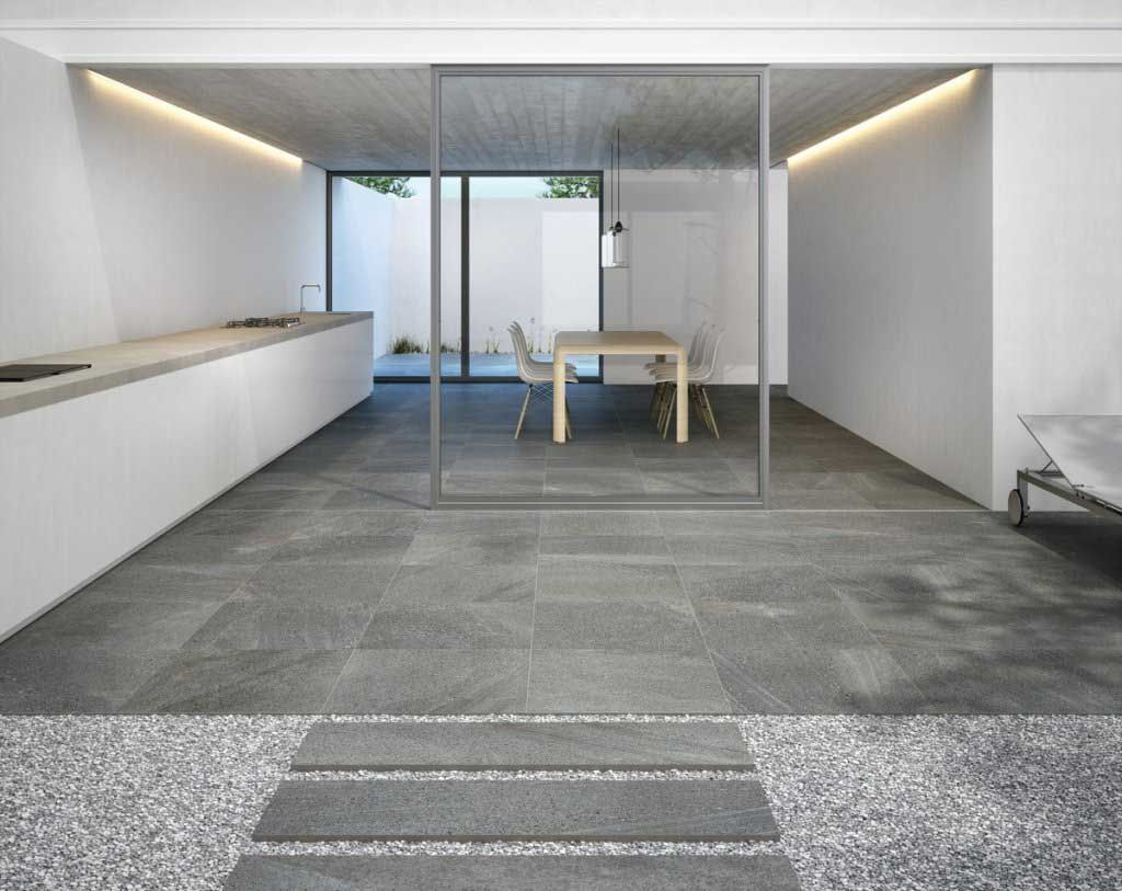 Cocina moderna y comedor con piso de baldosas de piedra, divisor de vidrio y vista al aire libre.