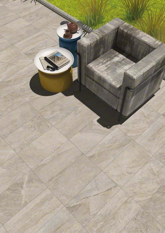 Patio con piso de baldosas, una silla y mesas pequeñas con artículos, césped al fondo.