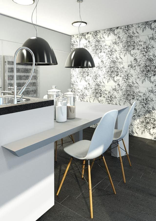Cocina moderna con encimera gris, sillas blancas y papel tapiz floral. Lámparas colgantes negras.