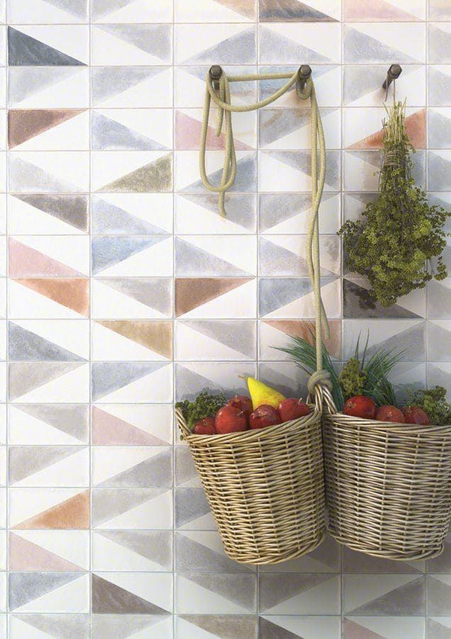 Dos cestas de mimbre con productos cuelgan de una pared con azulejos geométricos.
