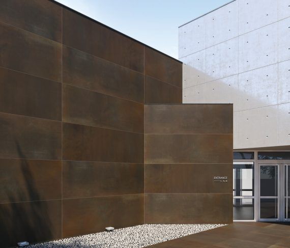 Exterior de un edificio moderno con paneles rectangulares marrones y paredes de hormigón blanco.