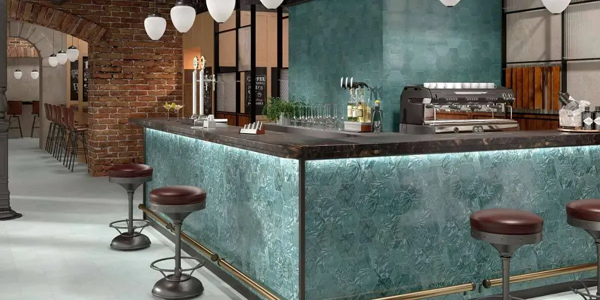 Interior de bar con frente color verde azulado, encimera de granito, taburetes y pared de ladrillos a la vista.