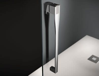 Manija de puerta de ducha cromada sobre un fondo gris oscuro y base de ducha blanca.