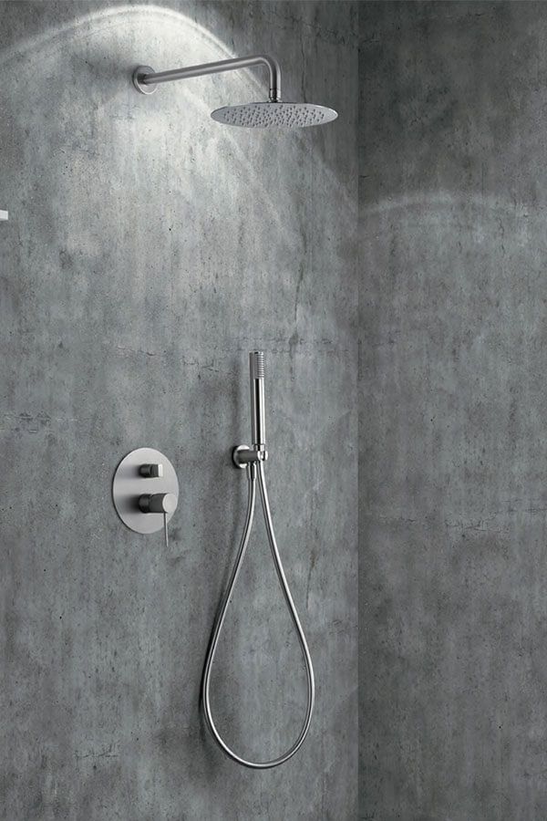Artefacto de ducha con cabezal de lluvia circular, ducha de mano y panel de control contra una pared de hormigón gris.