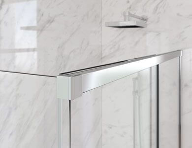 Primer plano de una puerta de ducha con marco plateado contra una superficie de mármol; el cabezal de la ducha es visible.