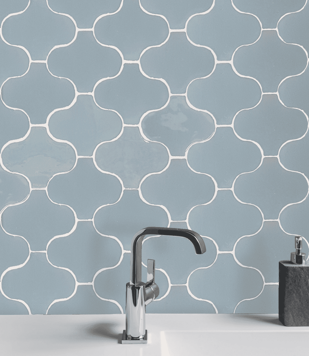 Salpicadero de azulejos decorativos azules con lechada blanca detrás de un grifo plateado y una encimera blanca.