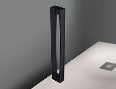 Manija de puerta rectangular negra sobre una superficie blanca, contra una pared gris.