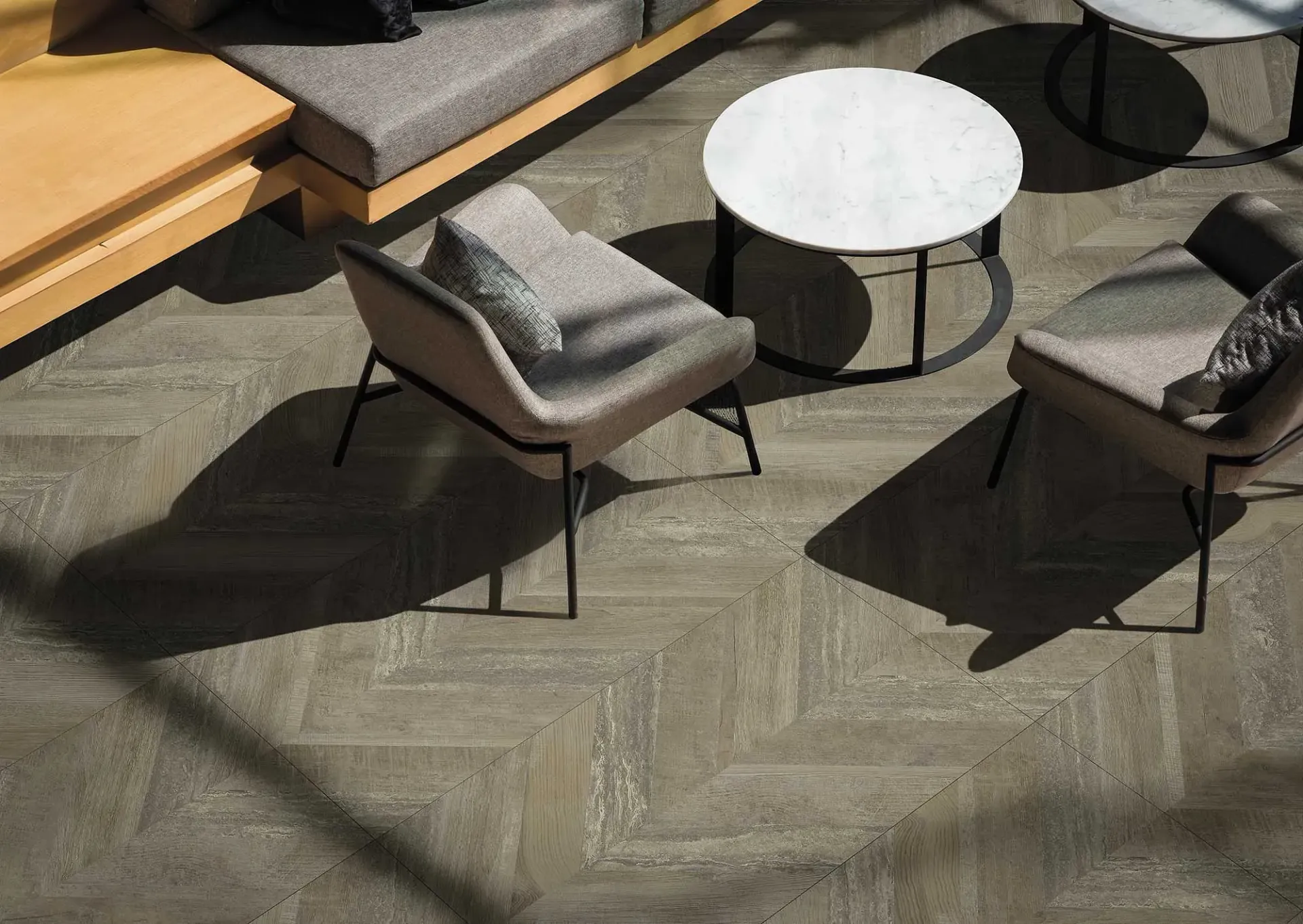 Zona de estar con sillas, mesa y suelo texturizado. Sombras desde arriba.