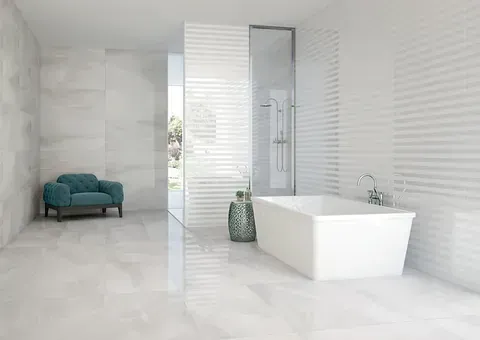Baño moderno totalmente blanco con bañera, ducha y sillón; detalle de pared texturizada, luz natural.