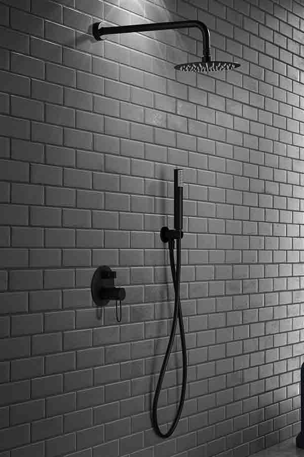 Accesorios de ducha negros sobre una pared de azulejos: cabezal de ducha tipo lluvia, ducha de mano y control de temperatura.